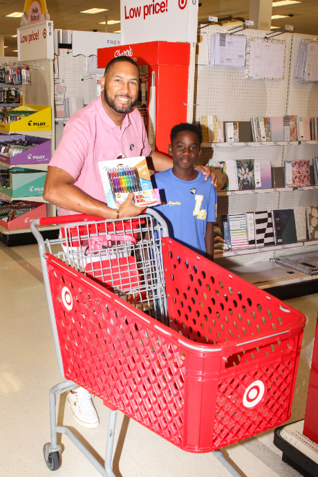 A Big and a Little pick out school supplies together during a back-to-school shopping event at Target, posing with a cart full of supplies.