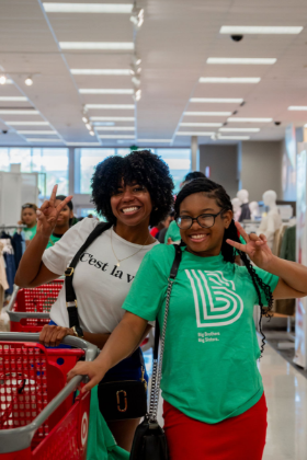 Two people, one a Big and the other a Little, smile and flash peace signs while shopping at Target during a back-to-school event.