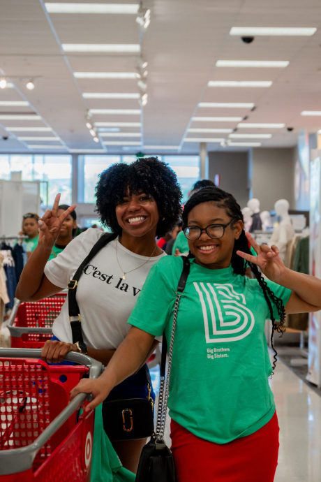 Two people, one a Big and the other a Little, smile and flash peace signs while shopping at Target during a back-to-school event.