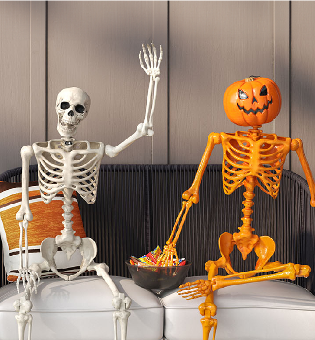 A decorative white skeleton and an orange skeleton with a jack-o-lantern head sitting on an outdoor couch.