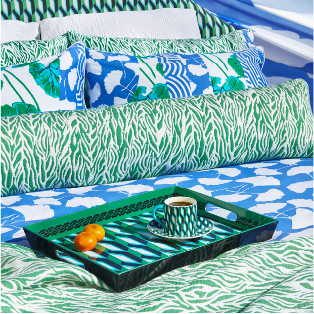 A bed, decorative pillows and a serving tray in bright blue and green contrasting patterns